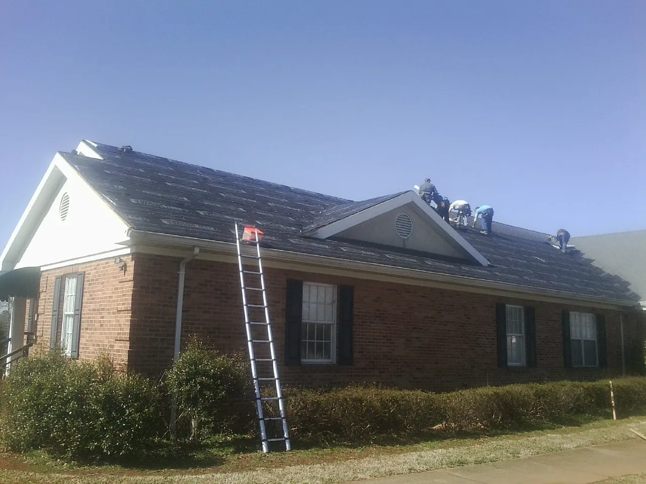 Crew tearing shingles off a brick ranch roof with a ladder set — Emergency Roof Repair work by our crew in Rossiter