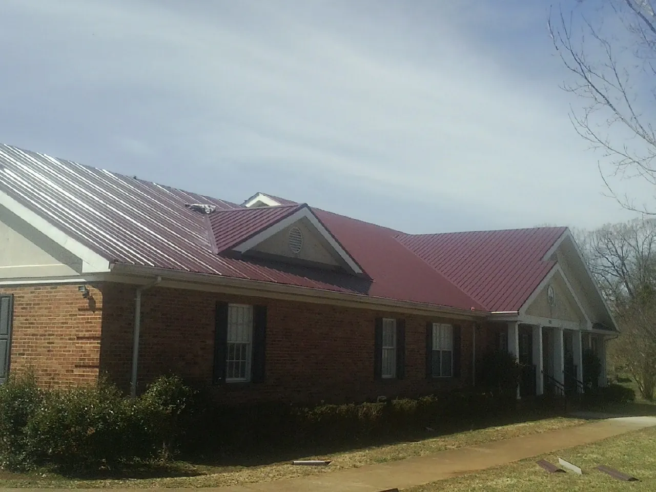 Red metal roof with gabled entries on a long brick building, from a Hail Damage Roof Repair job in Rossiter