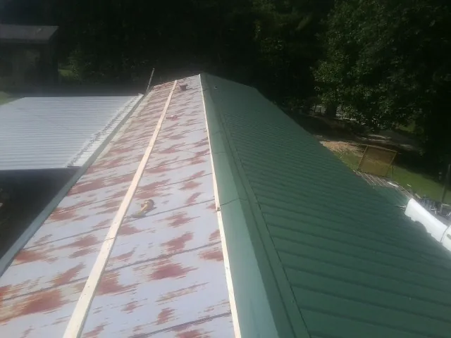 Old rusted panels beside newly installed green metal roofing — Wind Damage Roof Repair by Roofing Brothers in Rossiter