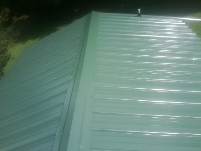 New green metal panels meeting at the ridge of a roof — Flat Roof Repair work by our crew in Rossiter