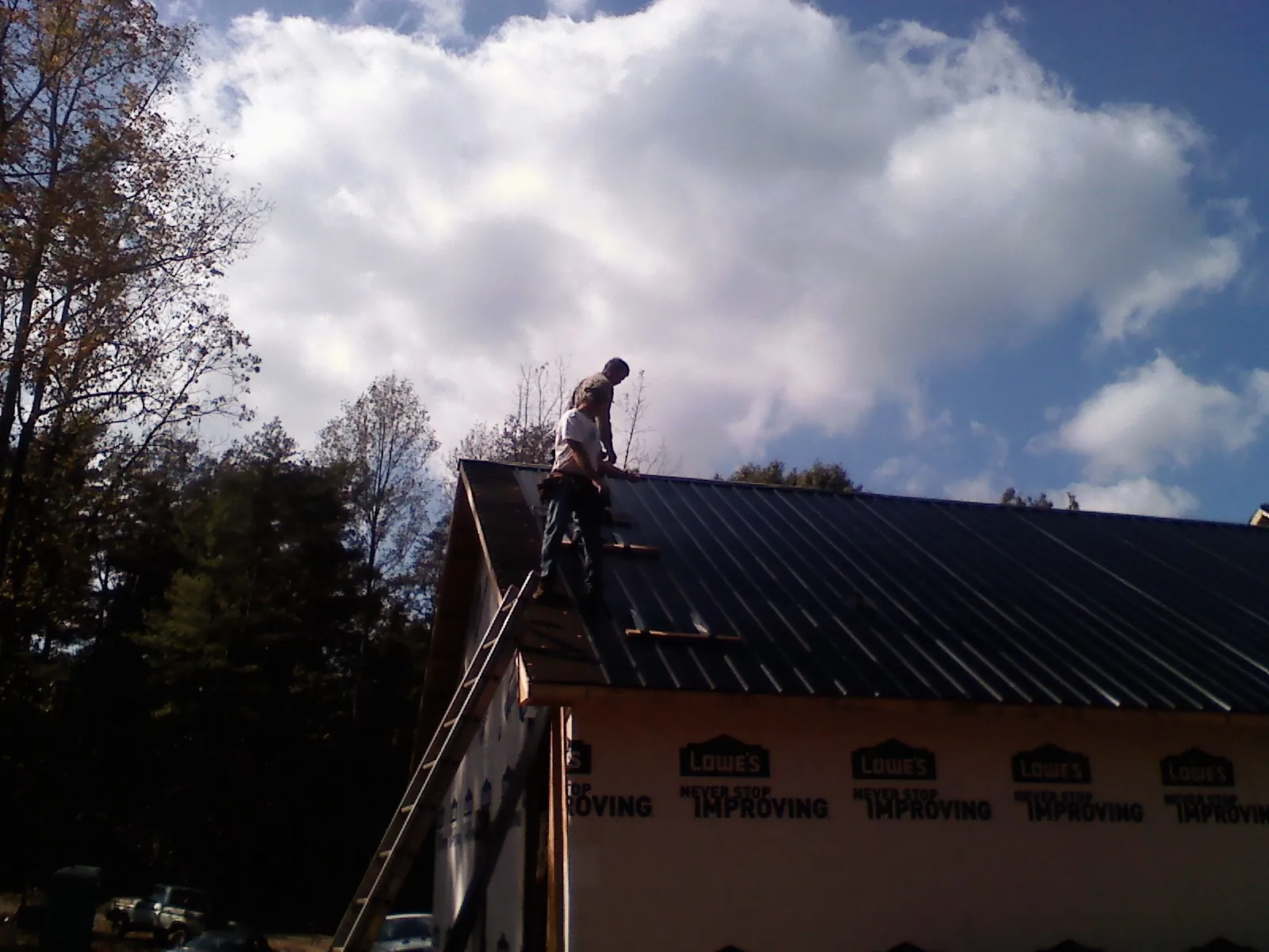 Roofer fastening dark metal panels high against a cloudy sky, from a Roof Inspection job in Rossiter
